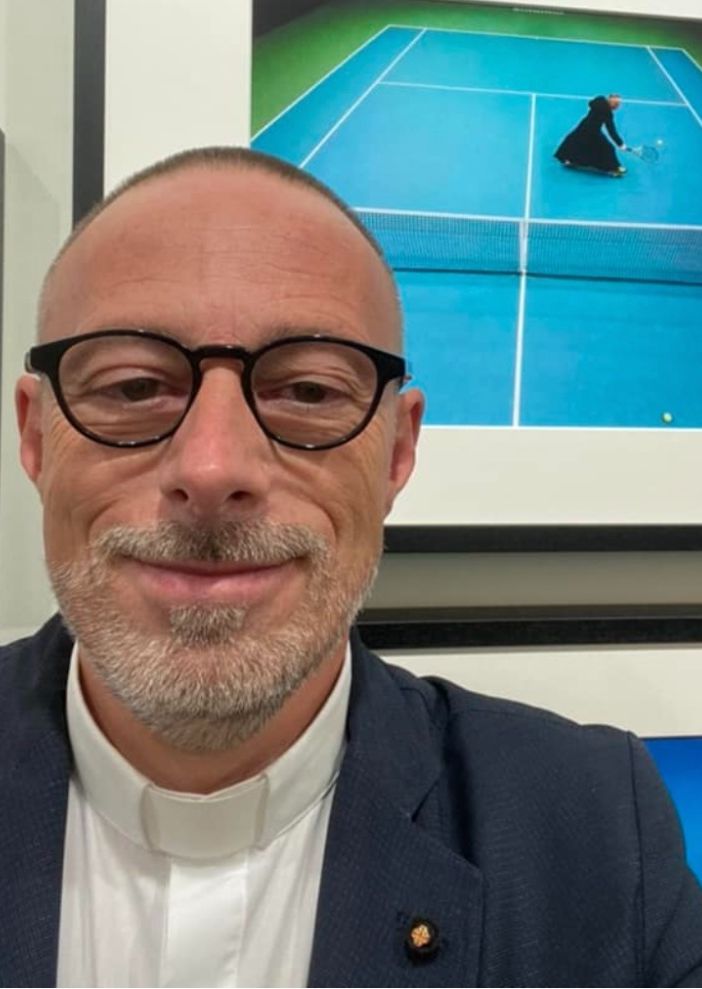 Don Paolo Bettonagli con alle spalle la foto scelta per la mostra di Guindani (foto dalla pagina Facebook di don Paolo)